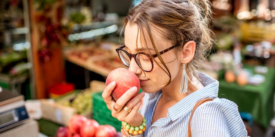 Une jeune femme sent un fruit dans un marché
