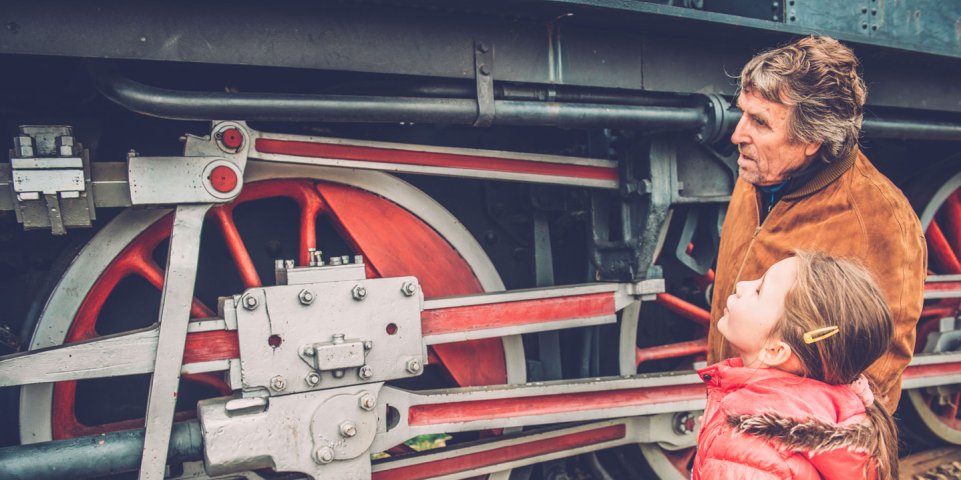Grand père et sa petite fille devant un train à vapeur