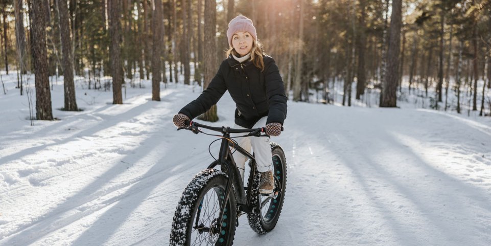Femme pratiquant le fatbike dans une forêt enneigée